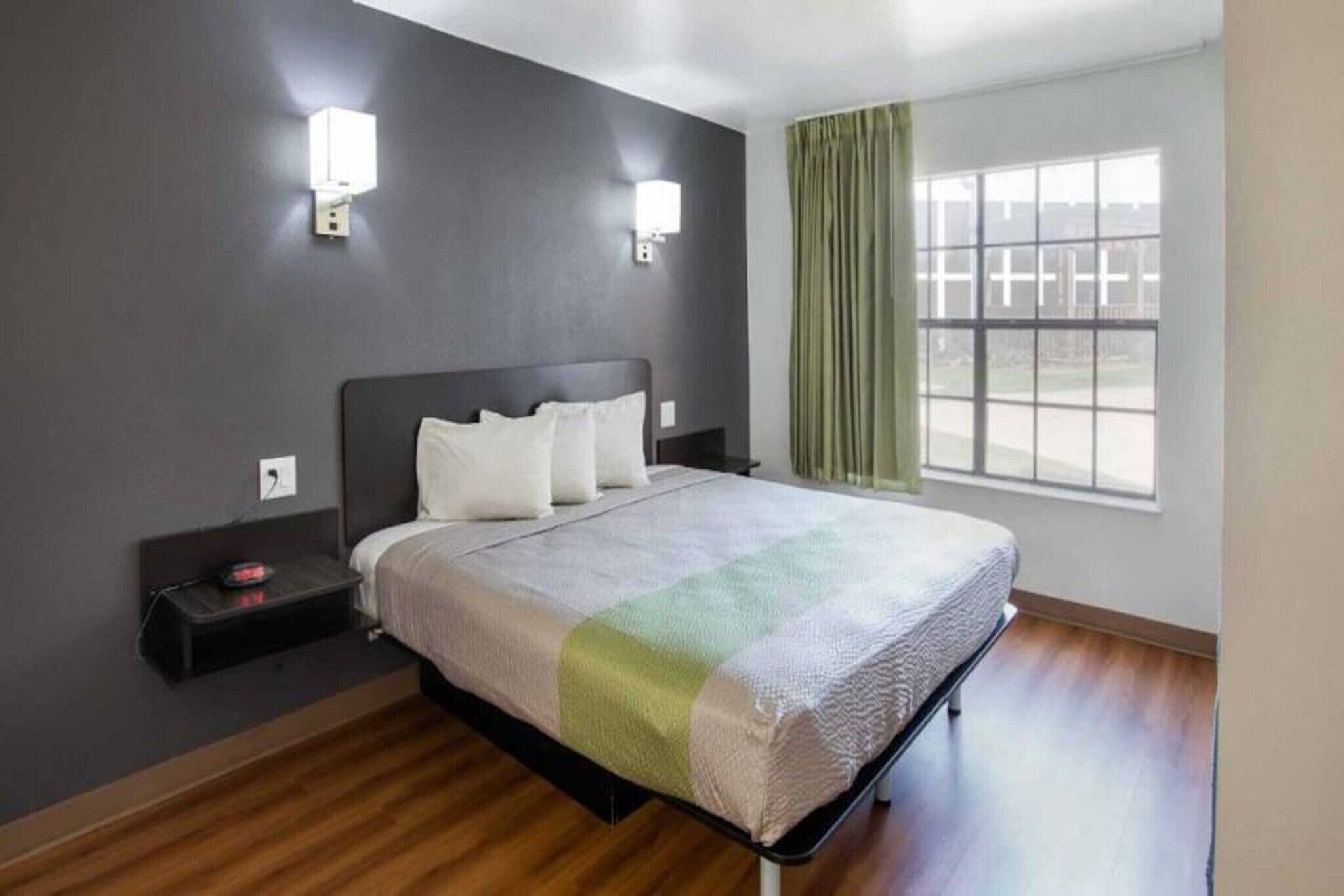 A hotel room with a bed, two bedside tables, a nightstand, a window with curtains, and a view of the outside.