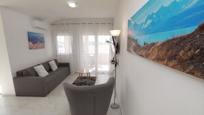 Ein Wohnzimmer mit grauem Sofa, einem kleinen runden Tisch, einer Stehlampe und einem großen Landschaftsbild an der Wand.