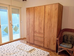 Ein Zimmer mit einem Holzschrank, einem Korbstuhl und einem Bett mit floralem Überwurf.