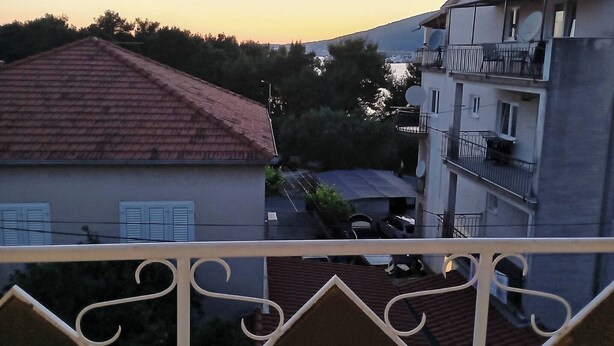 Ein Wohngebäude mit rotem Ziegeldach, Satellitenschüsseln und einem Balkon mit weißer Brüstung.
