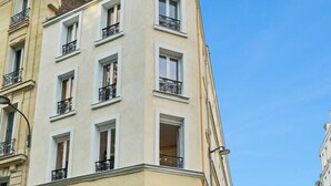 Un immeuble d’angle avec un commerce au rez-de-chaussée, de nombreuses fenêtres et une façade donnant sur la rue.