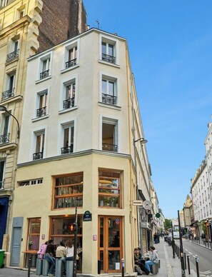 Ein Eckgebäude mit Laden im Erdgeschoss, mehreren Fenstern und einer sichtbaren Straße.
