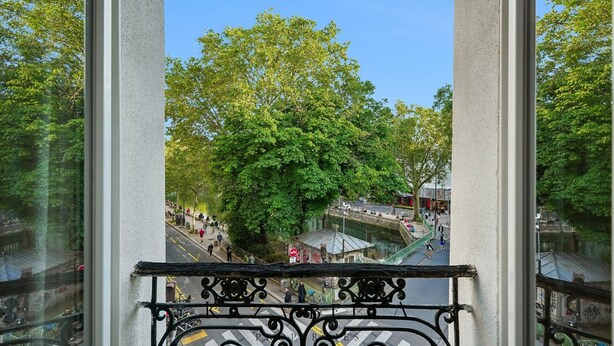 Un balcon donnant sur une rue bordée d’arbres et une zone piétonne.