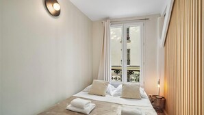 Une chambre d’hôtel avec un lit, une fenêtre avec des rideaux, un balcon avec une balustrade et un luminaire fixé au mur.