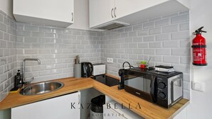 Une cuisine moderne avec des meubles blancs, un évier en acier inoxydable, un grille-pain, une bouilloire et un four à micro-ondes.