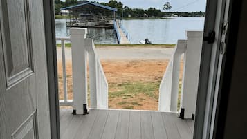 Uitzicht door een deur op een terras met uitzicht op een meer, met een overdekt gedeelte en een zandstrand.