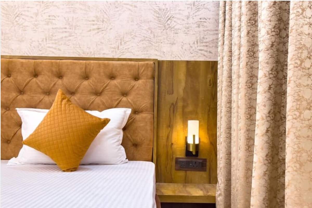 A bed with a tufted headboard, a bedside table with a wall-mounted light, and a patterned curtain.