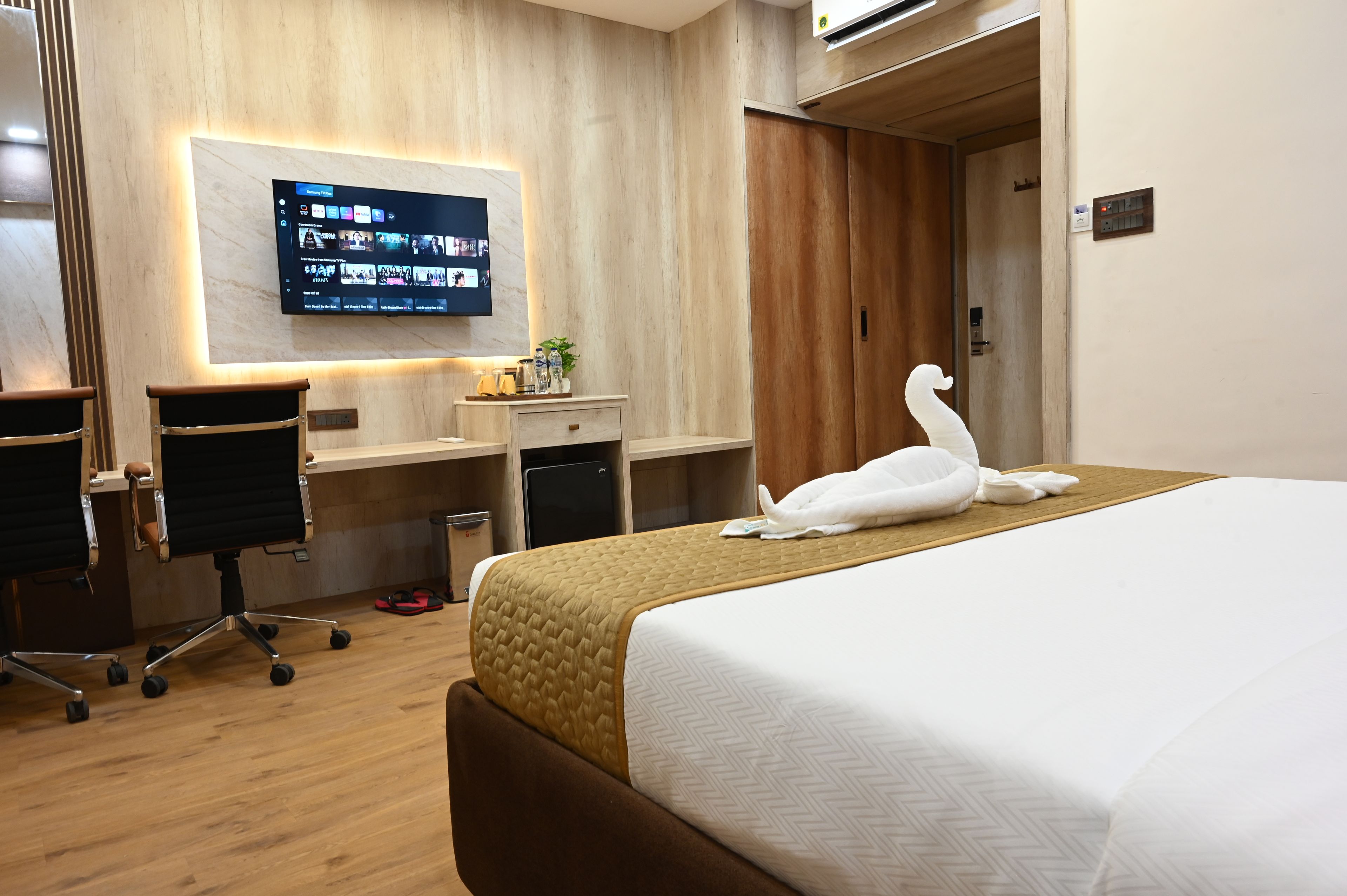 Habitación de hotel con cama, escritorio, silla, televisor montado en la pared y armario.