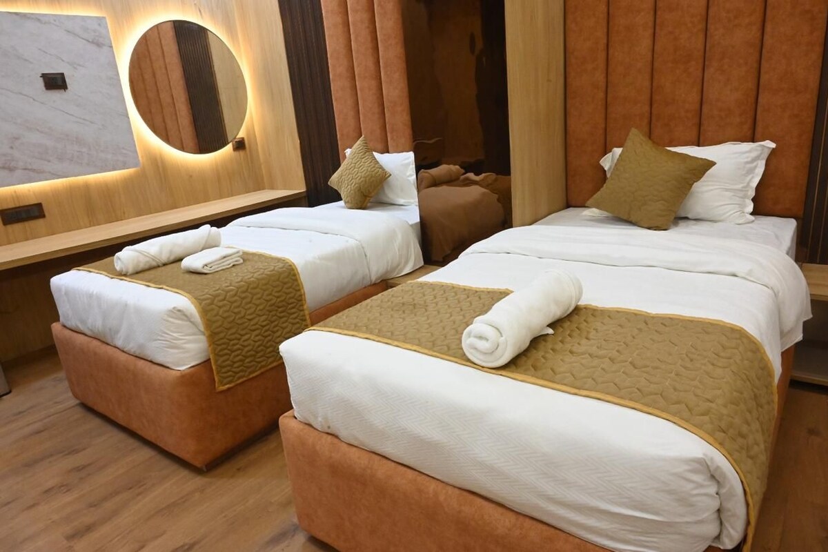 A hotel room with two beds, a large mirror, and a wooden floor.