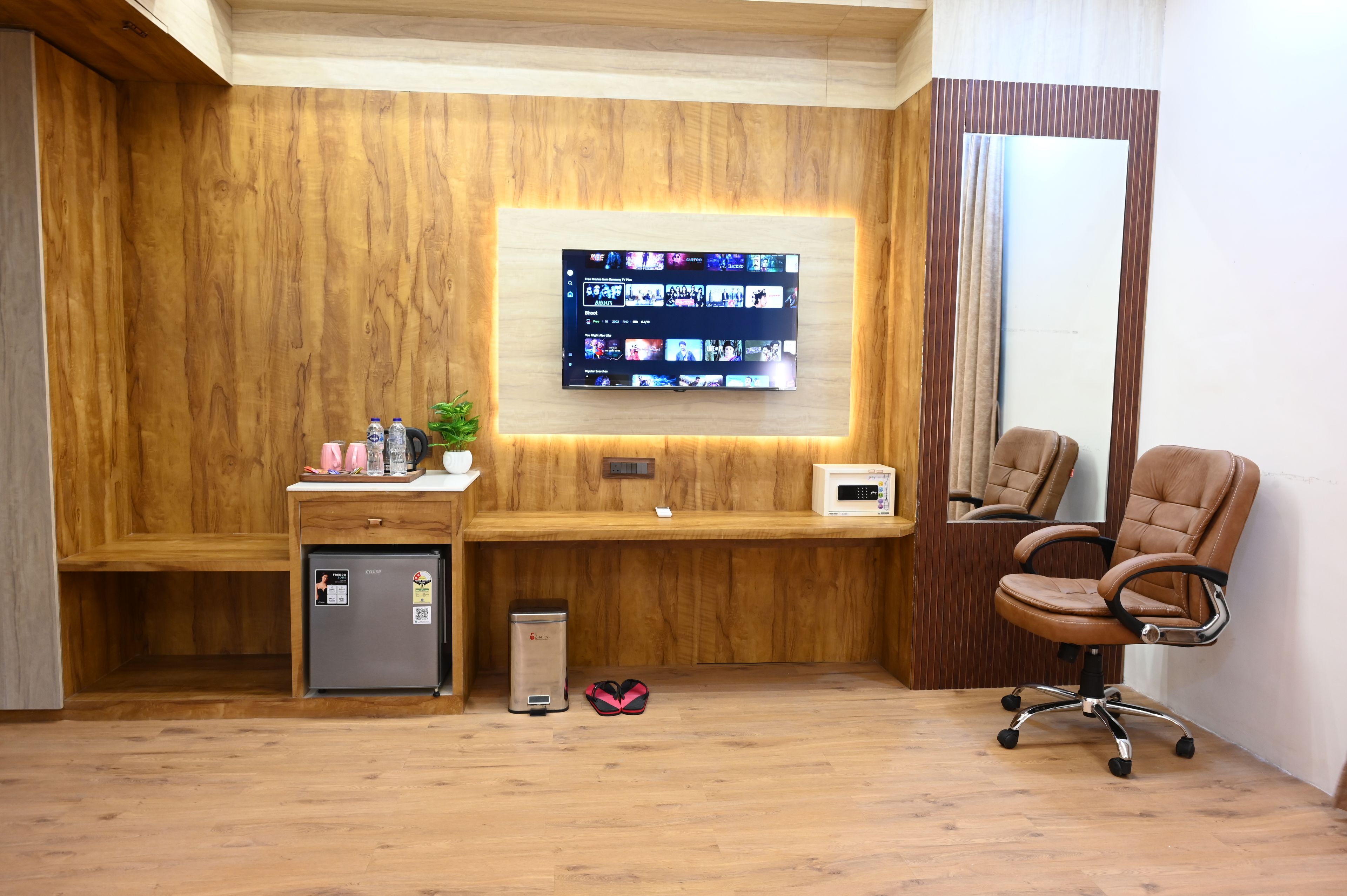 A modern office space with a wooden desk, a computer monitor, a chair, and a small refrigerator.