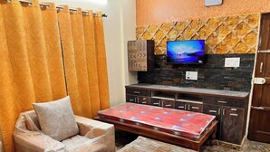 Un ambiente compatto con un divano, un piccolo tavolo, una TV e una parete con decoro effetto pietra.