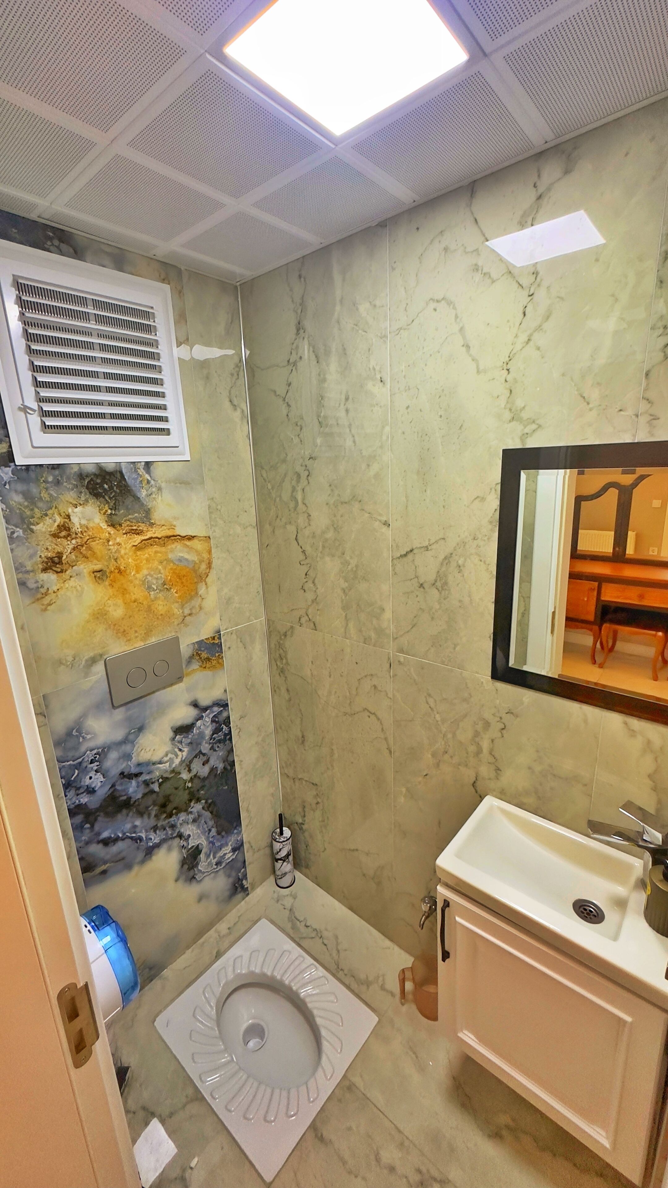 Une salle de bain avec un mur en marbre, des toilettes, un lavabo et un miroir.