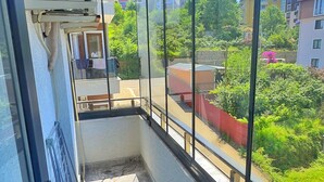 Un balcón con vistas a una zona residencial, una ventana con reja de metal y un equipo de aire acondicionado.