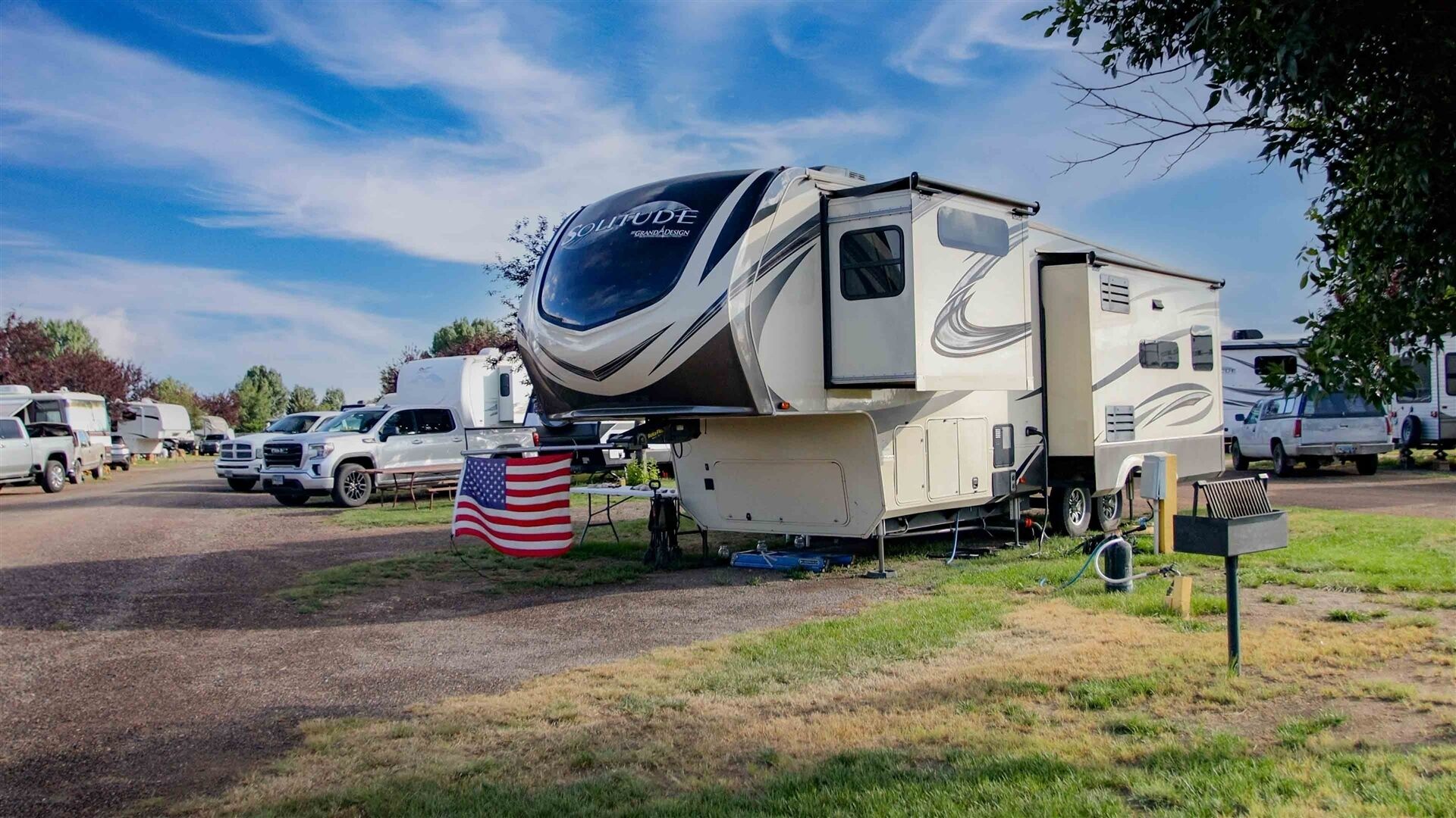 A recreational vehicle with a large awning, a flag, and a sign indicating 'Grand Design.'