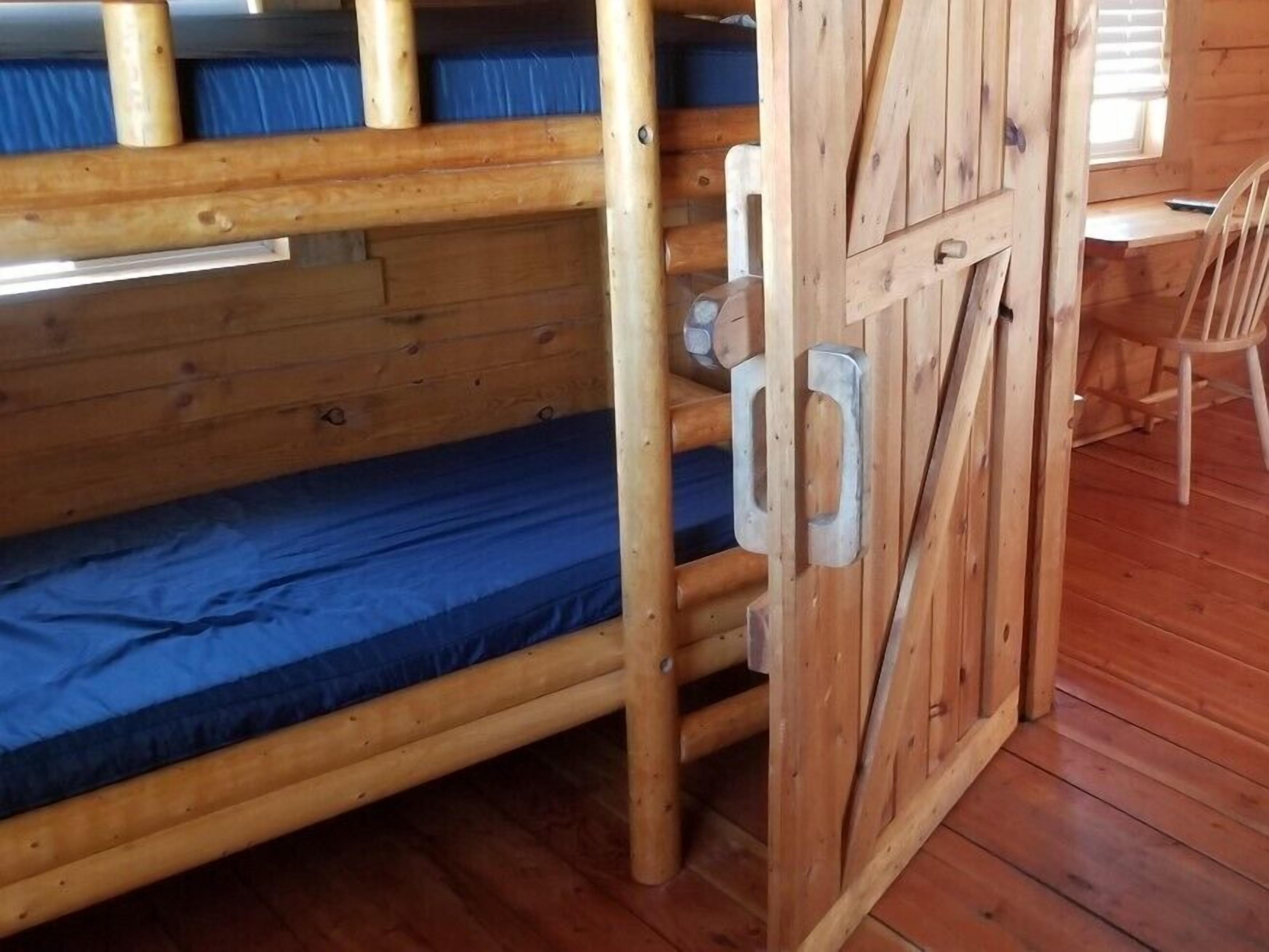 Una cama litera con estructura de madera y un cierre metálico, una silla y suelo de madera.