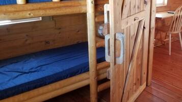 Una cama litera con estructura de madera y un cierre metálico, una silla y suelo de madera.