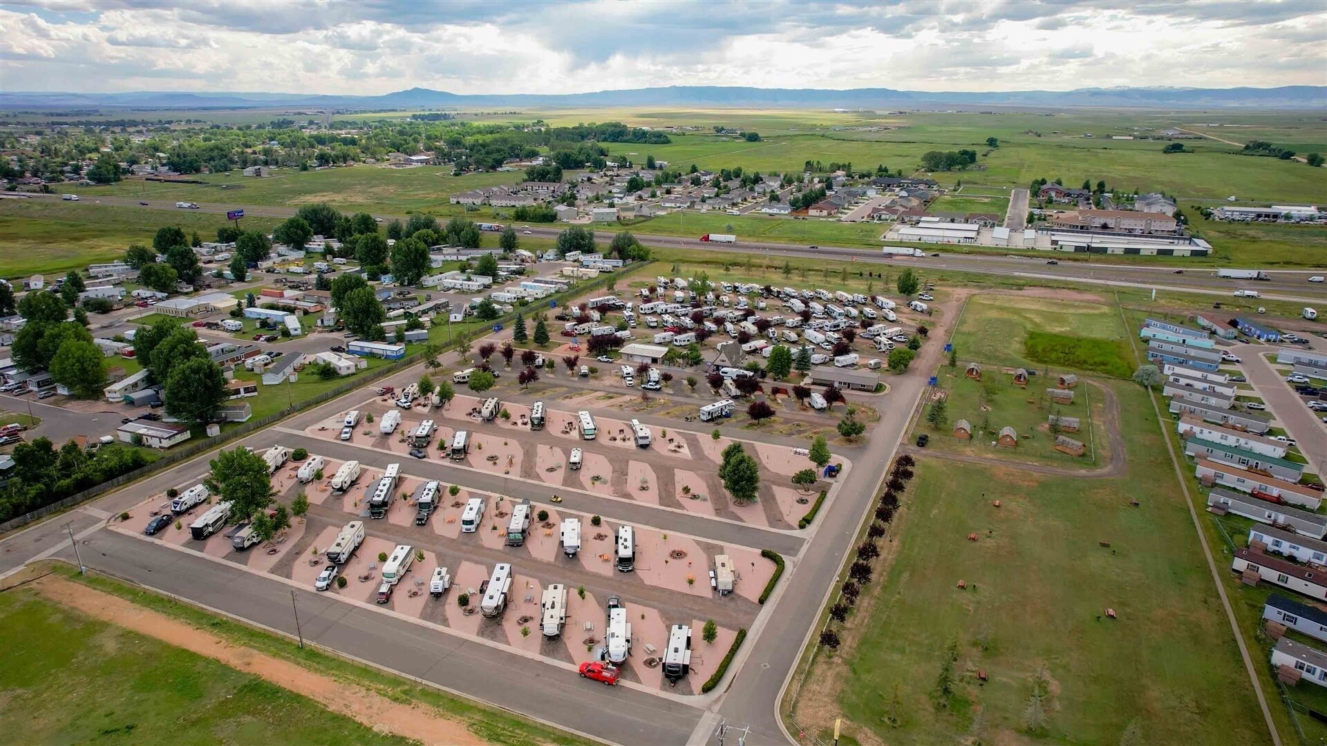 Ein Luftbild eines Campingplatzes mit Wohnmobilen, einem großen Parkplatz und umliegenden Grünflächen.