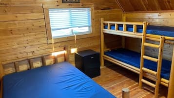 Una cabaña con literas, un pequeño calentador negro y una ventana con persianas.