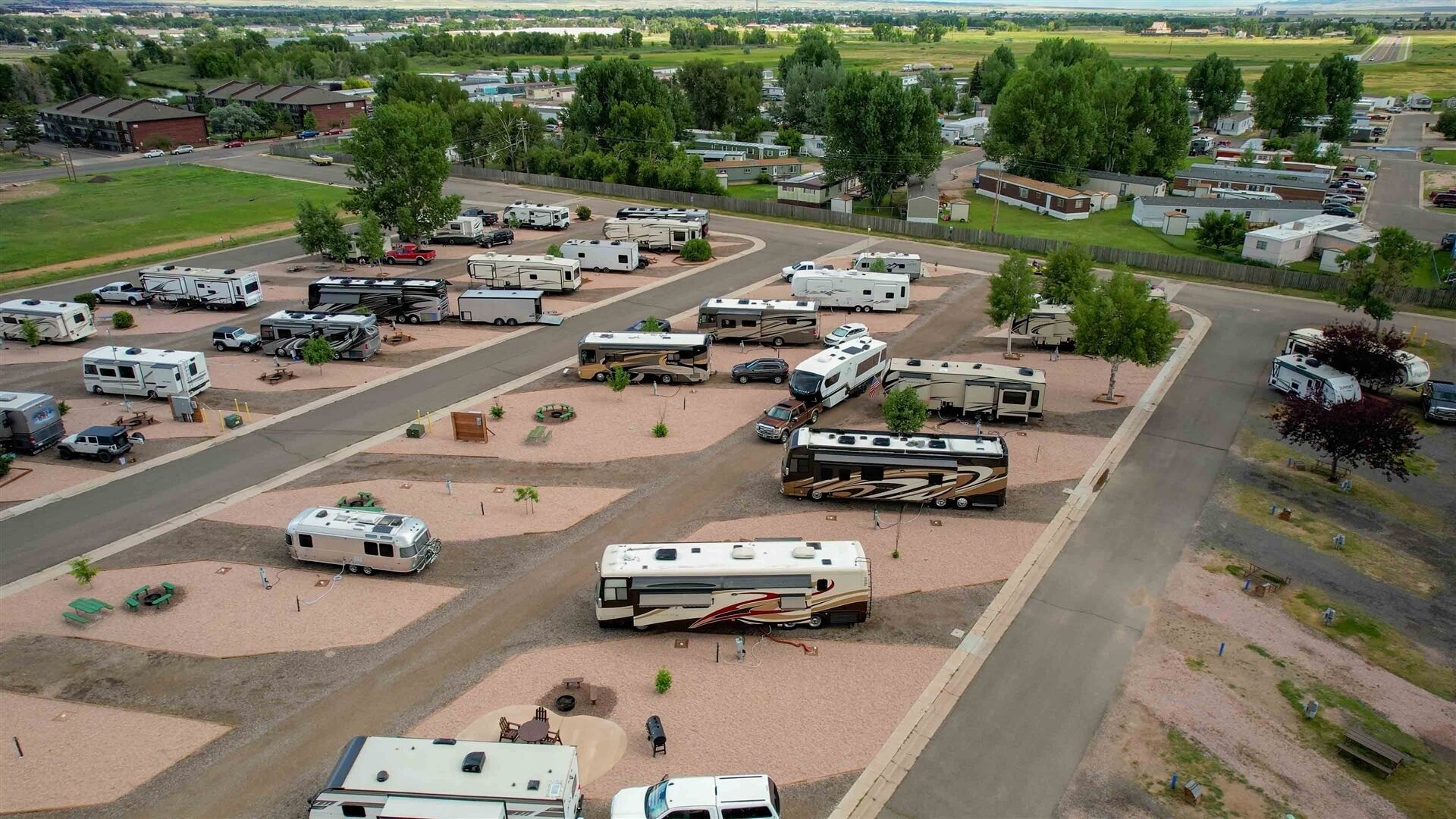A campground with RVs and trailers parked in designated areas, surrounded by trees and open fields.