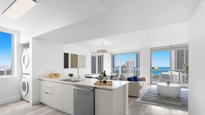 Een modern appartement met een keuken, eetgedeelte en woonruimte, met grote ramen en uitzicht op de stad en de oceaan.