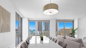 Een moderne hotelkamer met een grote eettafel, comfortabele zitplaatsen, een groot raam met uitzicht op de stad en een hangende lamp.