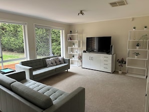 A living room with a grey sofa, a flat-screen TV, and white shelving units.
