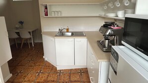 Cocina compacta con pileta, estufa y microondas. Hay una zona de comedor con sillas y una mesita.