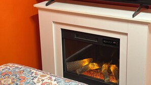 Una chimenea con un televisor encima, una mesa con diseño en frente y una pared naranja.