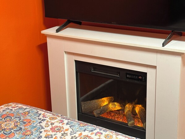 Une cheminée surmontée d’un téléviseur, une table à motifs placée devant, et un mur orange.