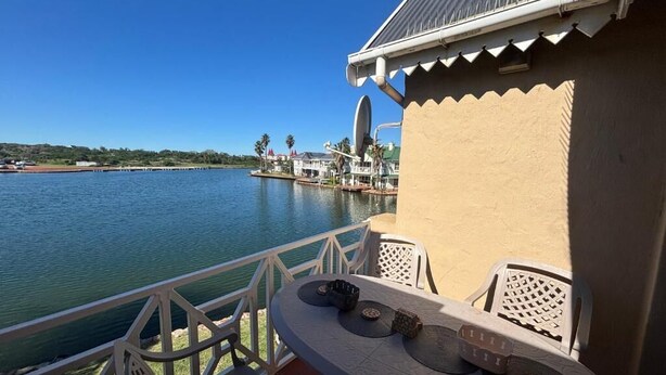 A balcony with a table and chairs overlooking a body of water, a building with a satellite dish, and a distant island with structures.