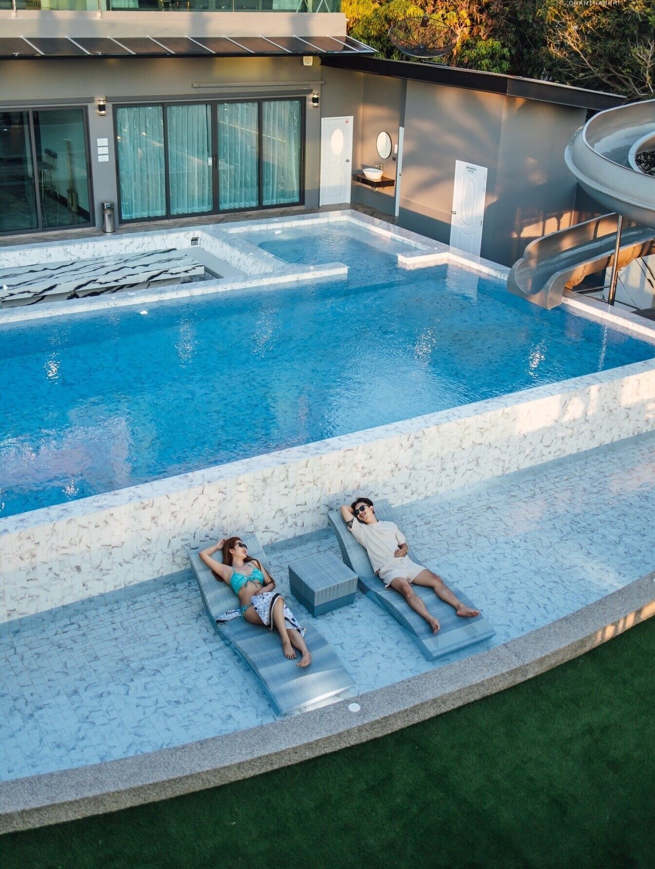 Ein Pool mit Glasboden, zwei Liegestühle und eine kleine Wasserfallanlage.