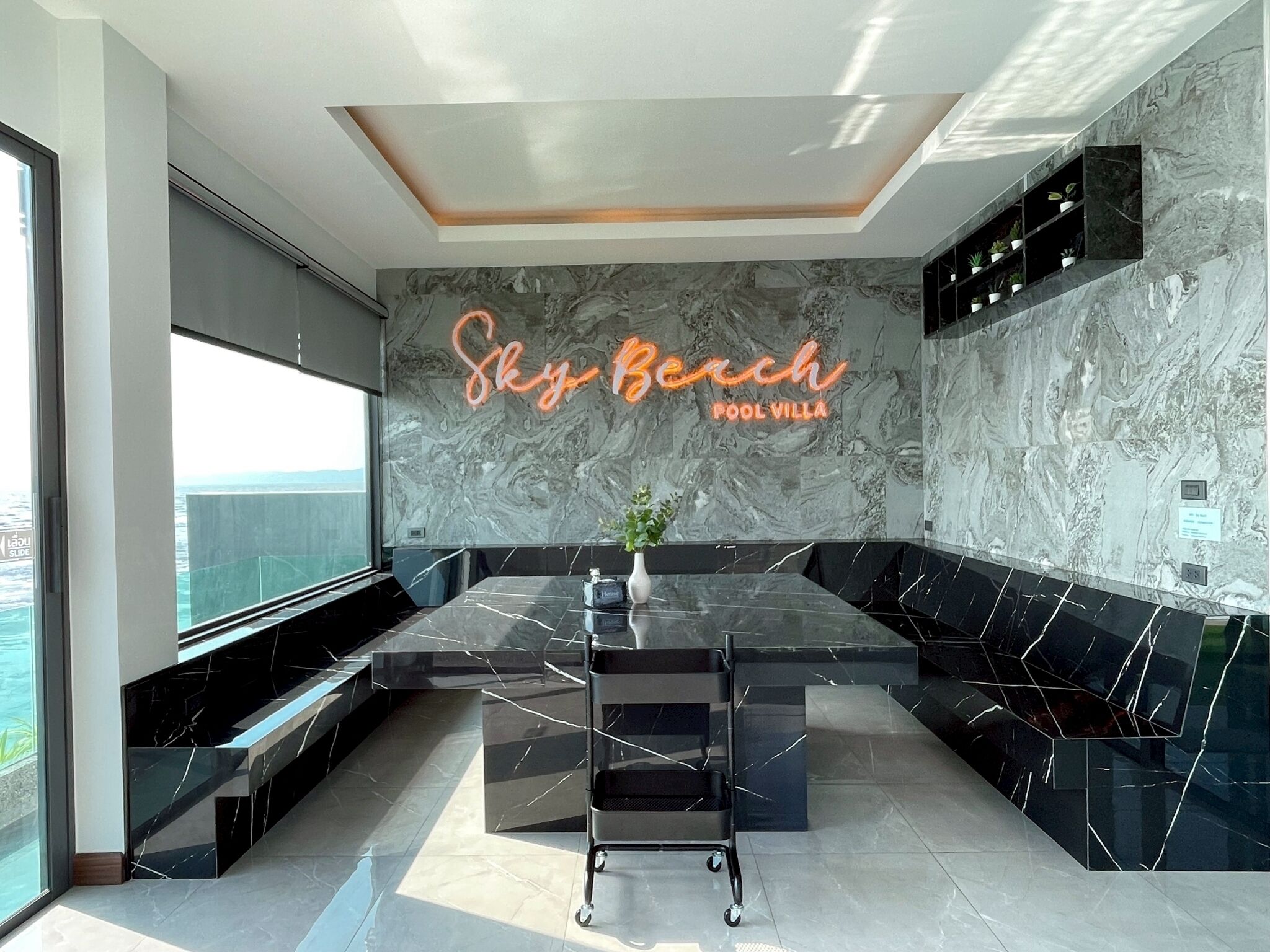 A modern kitchen with a marble backsplash, a neon sign reading 'Sky Bench Pool Villa,' and a view of the sea.