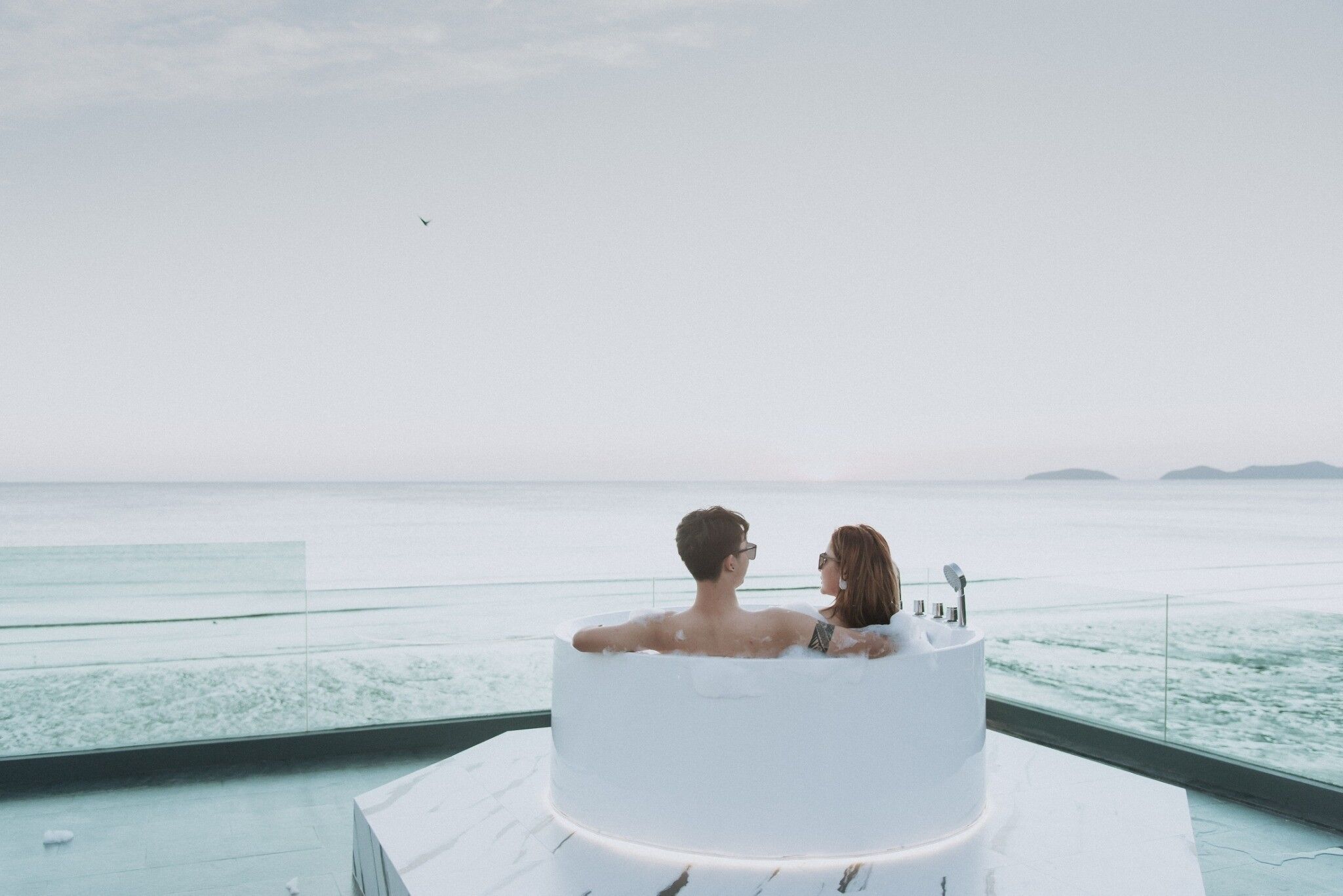 Una pareja en una bañera con vista a un cuerpo de agua y tierra distante.