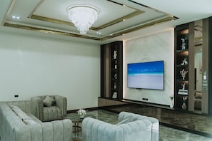A modern living room with a large flat-screen TV, a chandelier, and a marble floor.