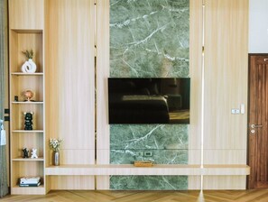 Una sala de estar moderna con un televisor de pantalla plana montado en una pared de mármol, estanterías de madera con objetos decorativos y una puerta de madera.