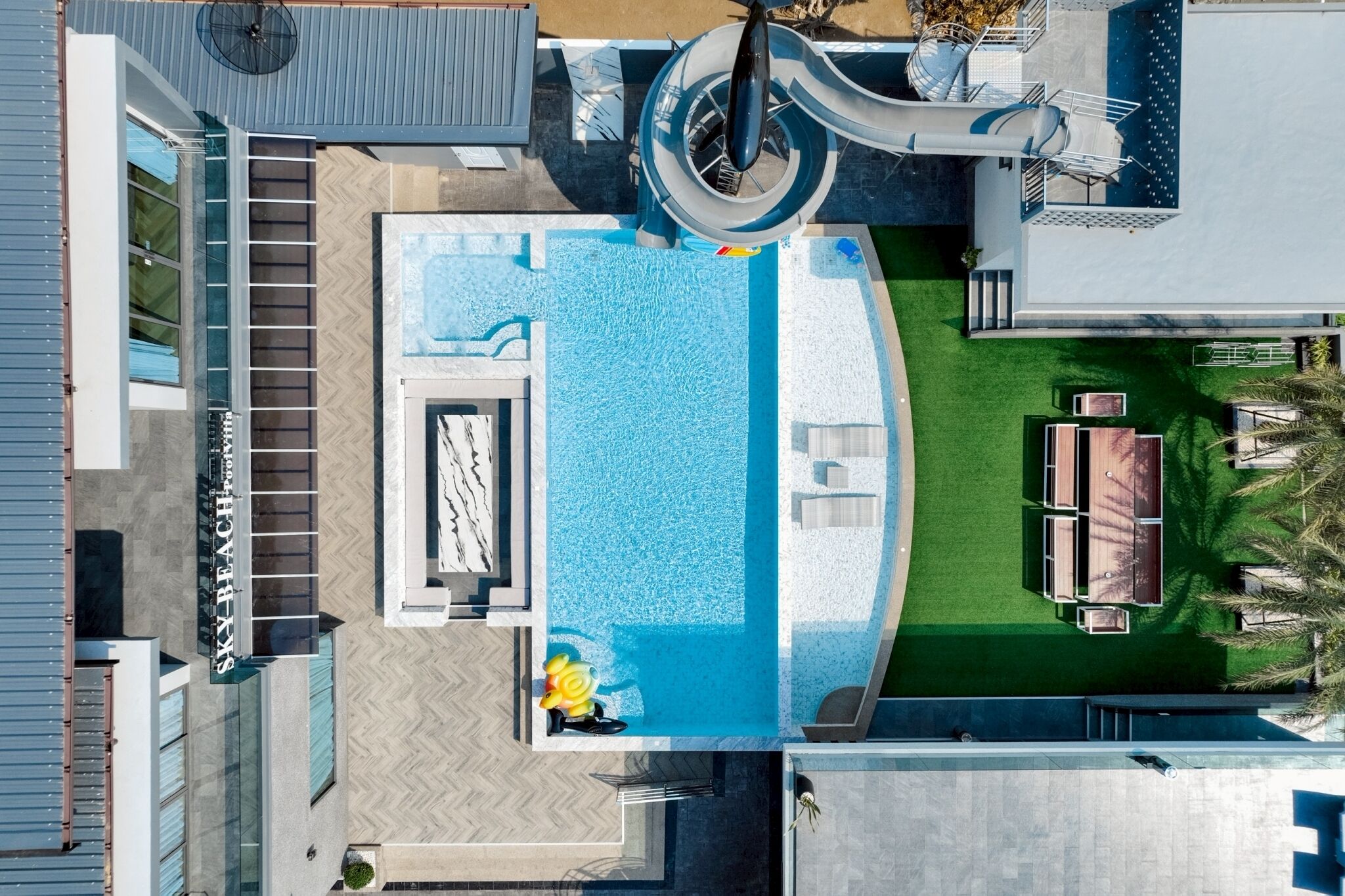 A rooftop pool with a slide, a sun lounger, and a small outdoor seating area.