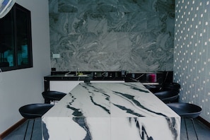 A modern kitchen with a marble countertop, black chairs, and a backsplash with a marble pattern.