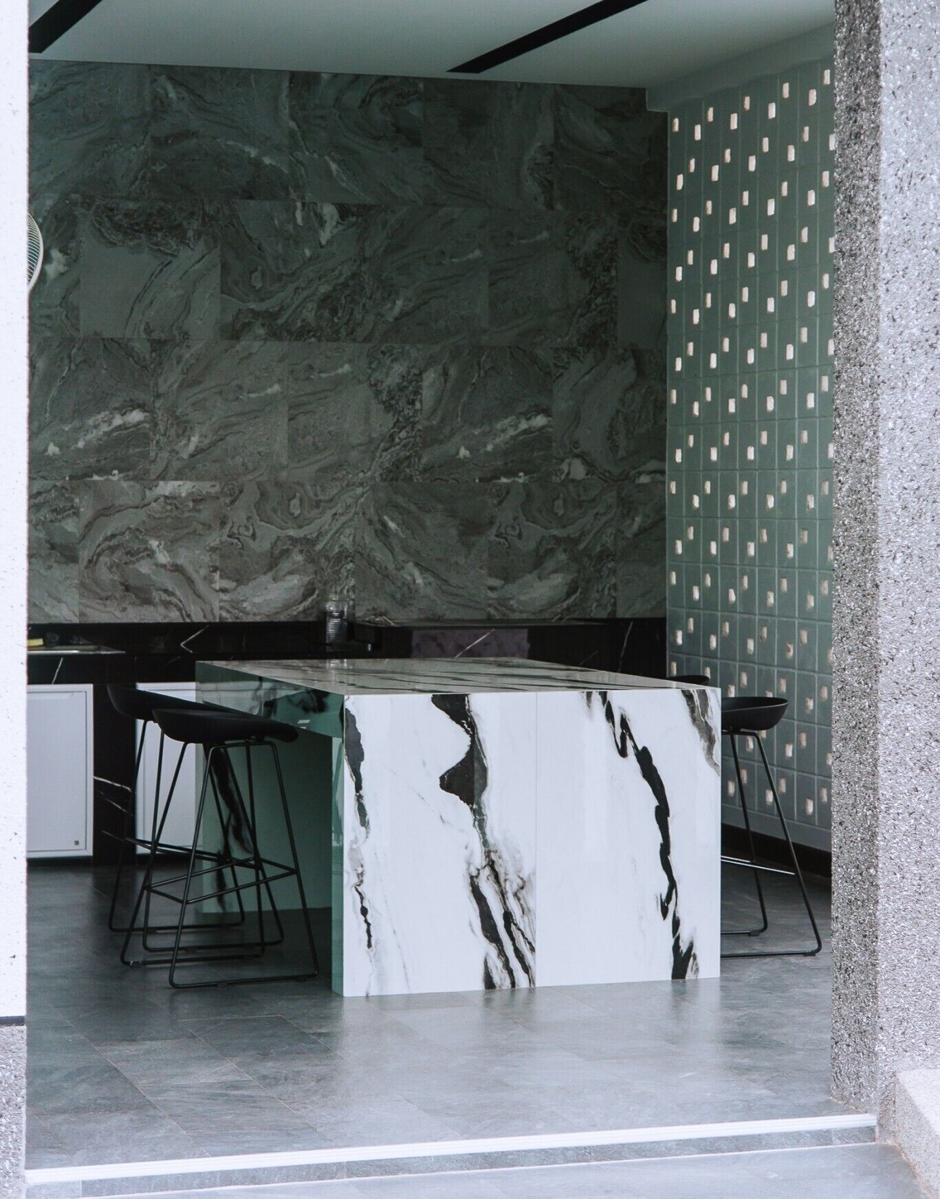 A modern kitchen with a marble countertop, black bar stools, and a patterned wall.