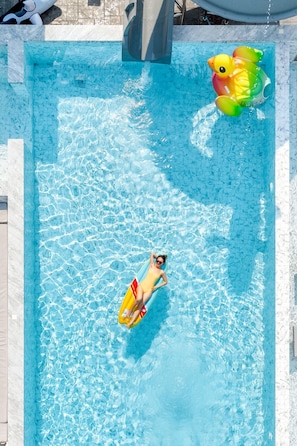 A rectangular swimming pool with clear blue water, a person floating on a yellow float, and a large inflatable duck toy.
