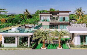 A modern multi-story hotel with a rooftop pool, glass railings, and a view of the surrounding greenery.