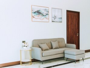 Una sala de estar moderna con un sofá color beige, una pequeña mesita de noche con un jarrón de flores y dos cuadros en la pared.
