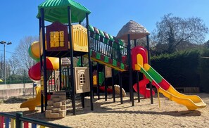 Ein Spielplatz mit Rutsche, Klettergerüsten und einem überdachten Spielbereich.