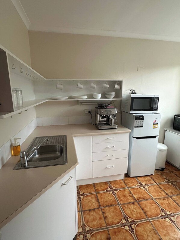 Eine kleine Küche mit Spüle, Kaffeemaschine, Mikrowelle und Kühlschrank.