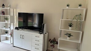 A living room with a flat-screen TV on a white cabinet, surrounded by white shelving units with potted plants. - Cozy Curtin- 3 guests house (Curtin)