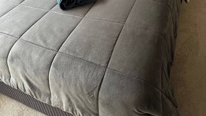 Un lit bien fait, avec une couette grise, une tête de lit grise et deux oreillers blancs.