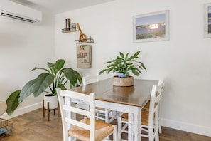 Un coin repas avec une table en bois, des chaises blanches et des plantes en pot.