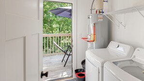 Een wasserette met een wasmachine en droger, een deur naar een balkon en een kleine prullenbak.