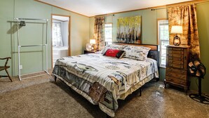 Une chambre à coucher avec un lit, une commode, un ventilateur et un tableau accroché au mur.