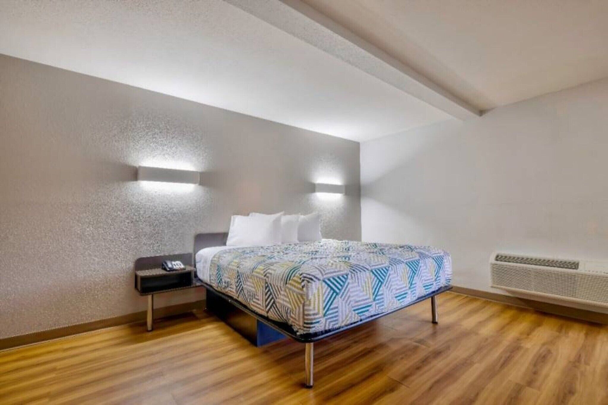 Un dormitorio con cama, mesita de noche, luces en la pared y un equipo de aire acondicionado.