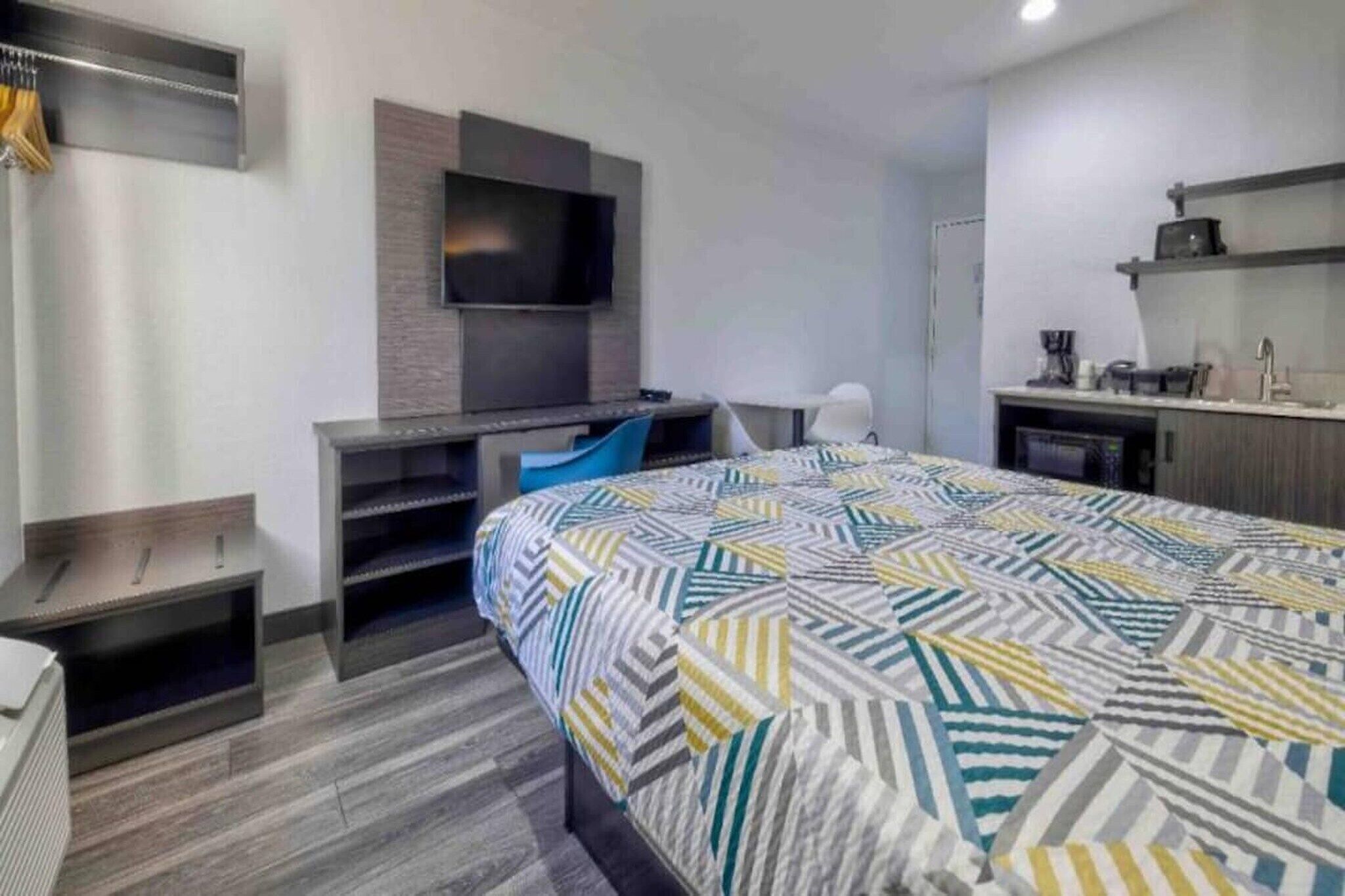 Ein modernes Hotelzimmer mit Bett, Schreibtisch mit Stuhl, einem wandmontierten Flachbildfernseher und einer Küchenzeile.